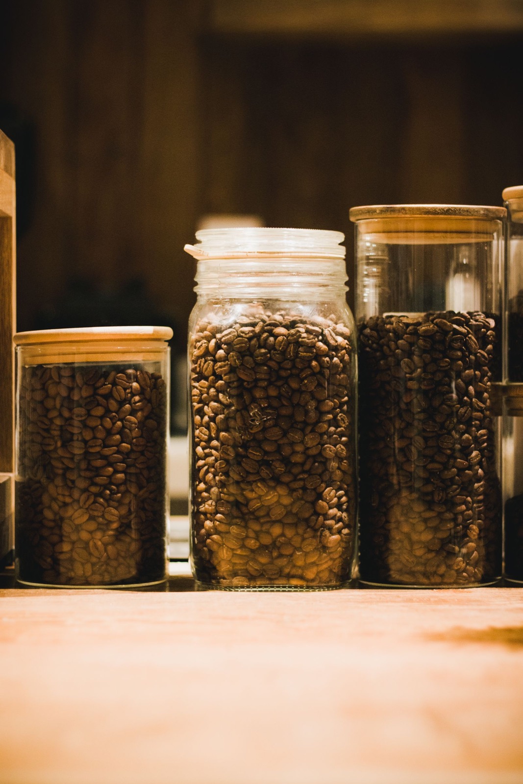 Roasted coffee beans stored in glass jars on a warm wooden surface