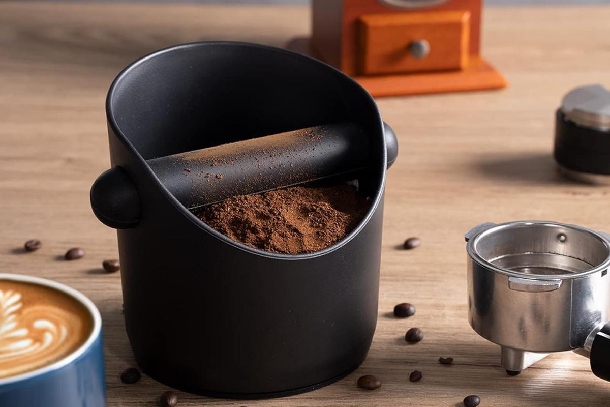 Black coffee knock box beside a portafilter and freshly made latte