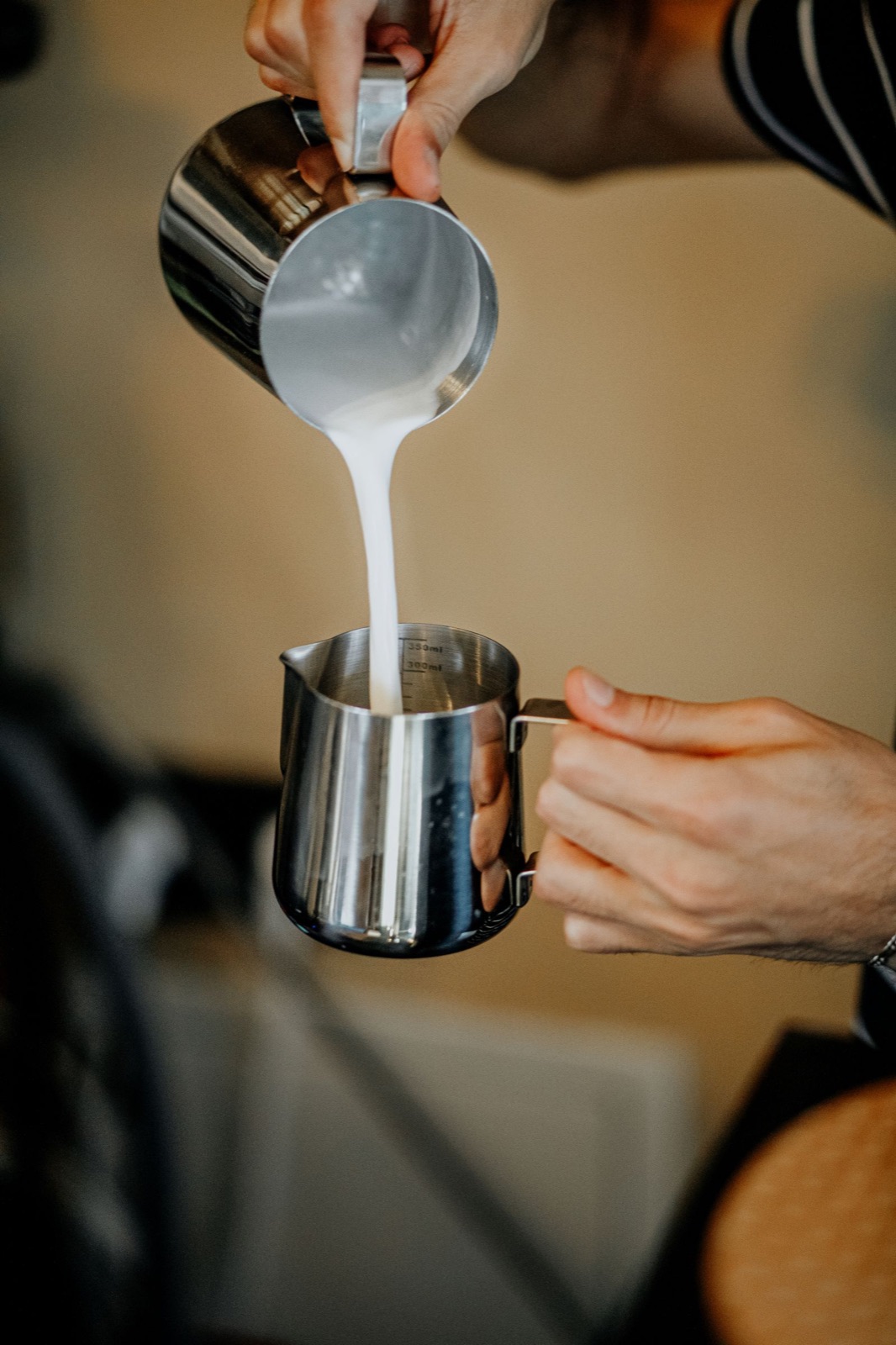 Barista texturing milk in two stainless-steel frothing pitchers