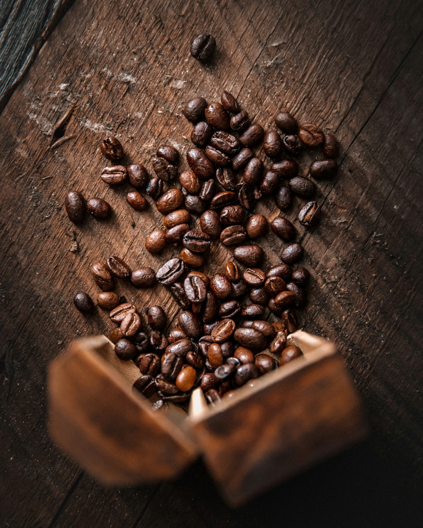 Roasted coffee beans scattered from a paper bag on a wooden surface