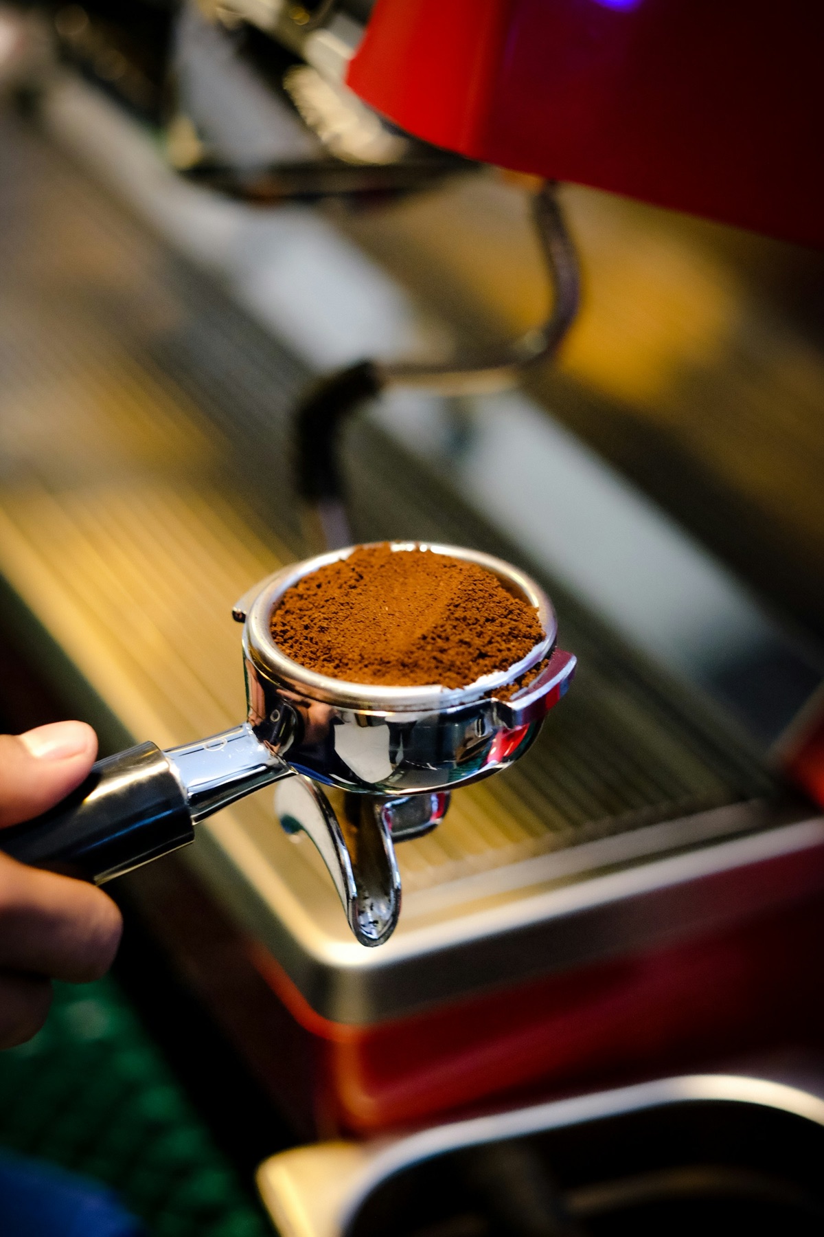 Freshly ground coffee levelled in a metal espresso portafilter beside a coffee machine